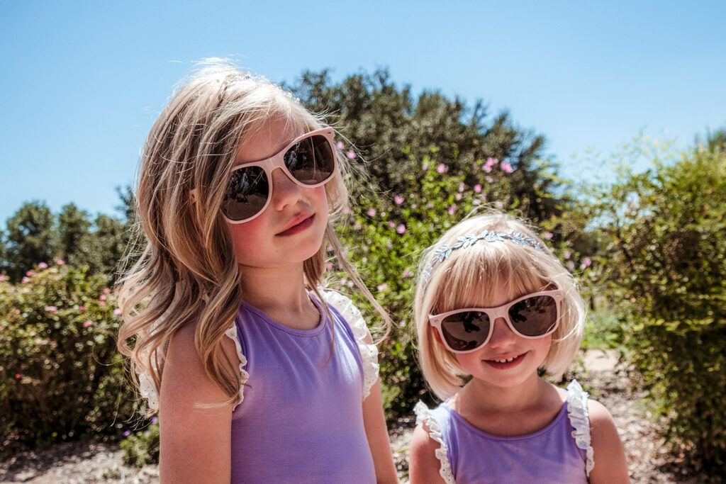 Photo of two girls wearing sunglasses and purple dresses a a hot summer Texas wedding.