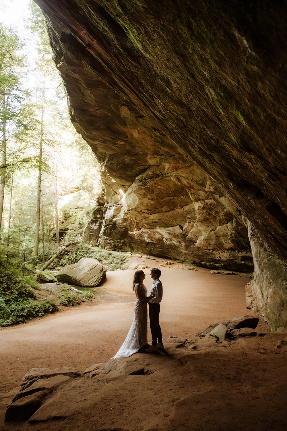 Option 1 (Dramatic & Descriptive):
A striking silhouette of a couple exchanging private wedding vows inside the massive recess of Ash Cave. The dark figures of the couple are framed against the bright, sunlit forest visible from the cave entrance during a summer elopement.