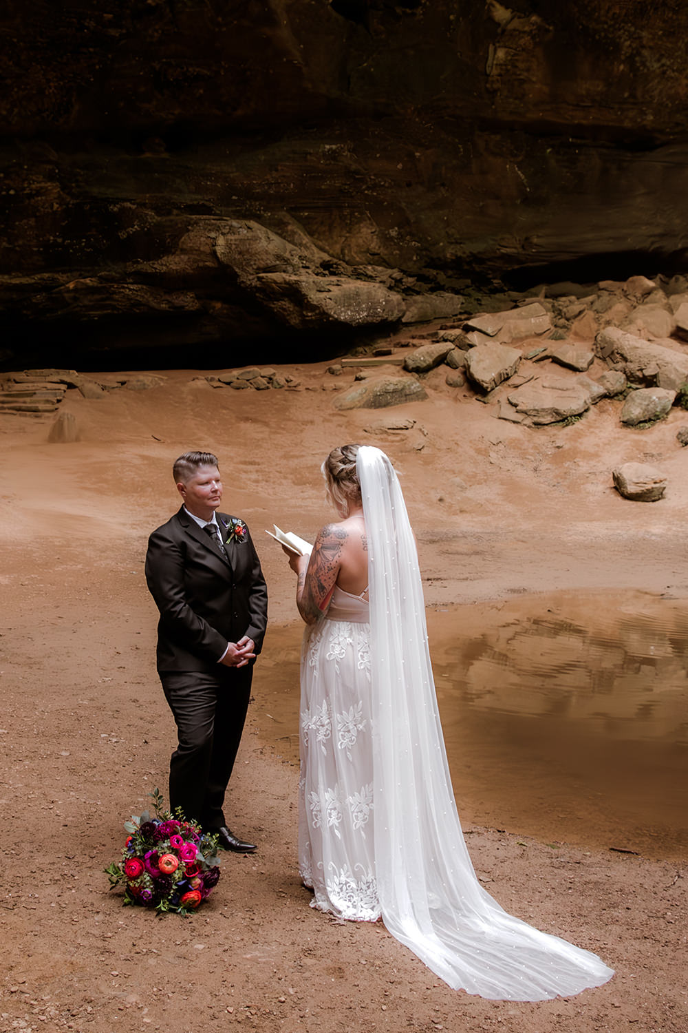 A queer couple exchanging private vows during an elopement at Ash Cave in Hocking Hills, Ohio. The scene captures an intimate moment of connection within the iconic natural landmark.