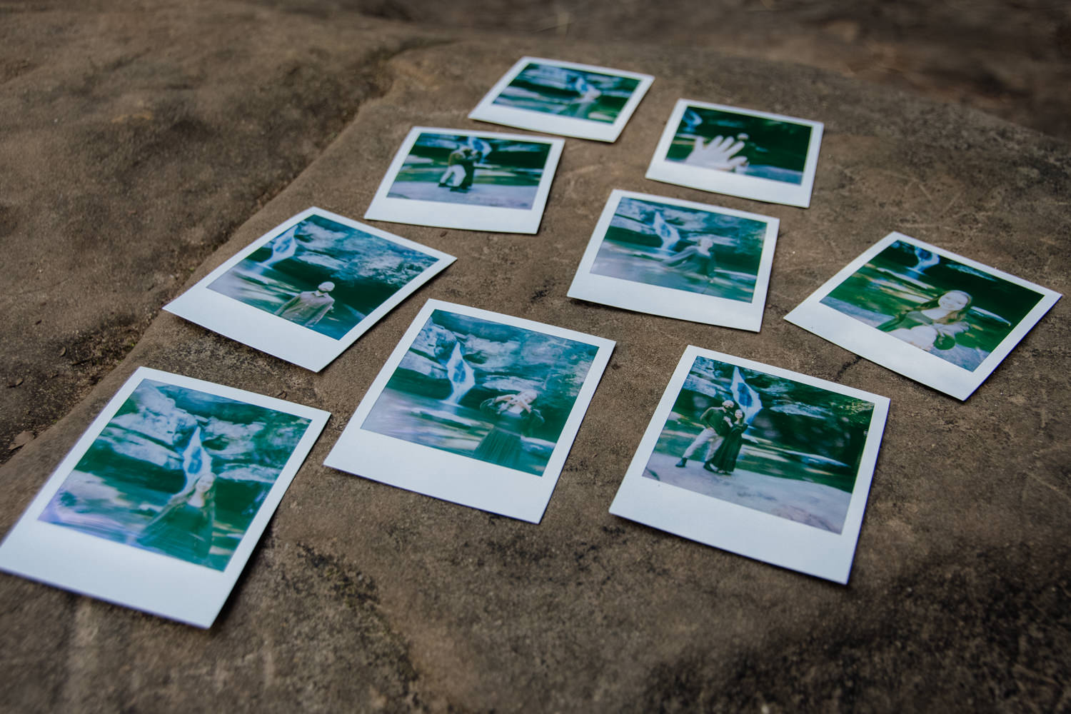 An overhead, close-up shot of two people sitting together, holding a small, square Polaroid photo. In the film's frame, a woman smiles while framing a heart shape with her hands against a backdrop of spring forest greenery. The Polaroid is placed in a heart carved into the sandstone.