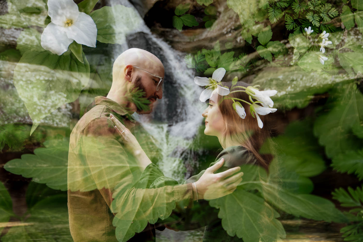 A double exposure of an engaged couple standing before the rushing white water of Cedar Falls in Hocking Hills. The image is layered with delicate spring ephemeral wildflowers, creating a translucent, magical fairytale effect where the couple and the forest seem to merge into one mystical scene.
