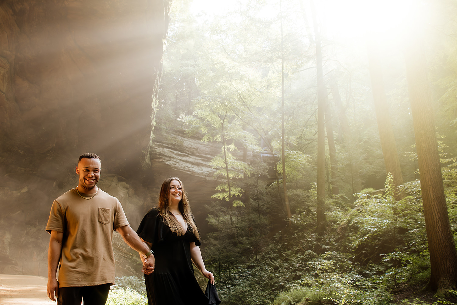 Rays of light shine down on a couple as they hold hands and walk out of Ash Cave in the Hocking Hills.