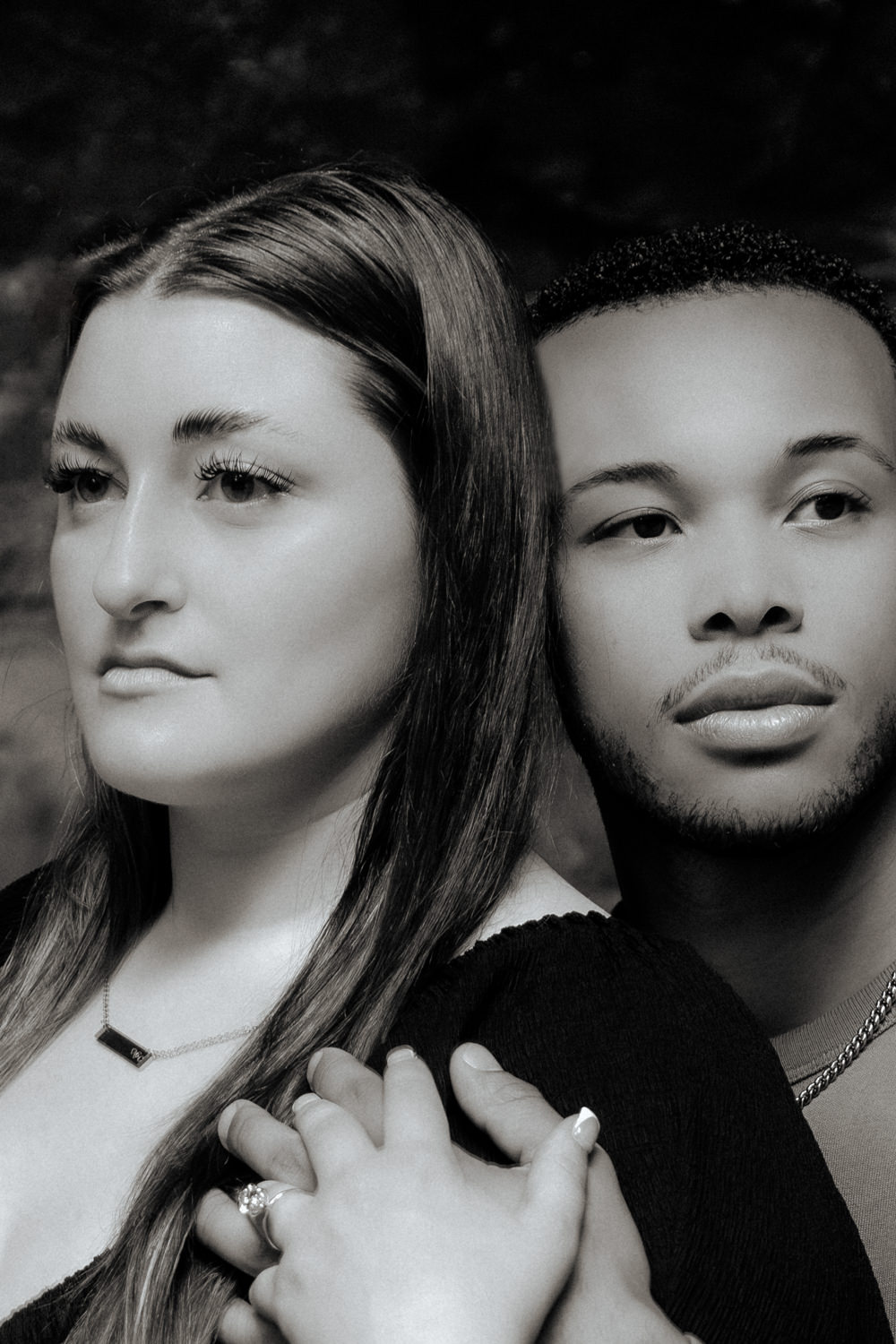 An intimate portrait of a white woman and a black man embracing but each looks in a different direction.