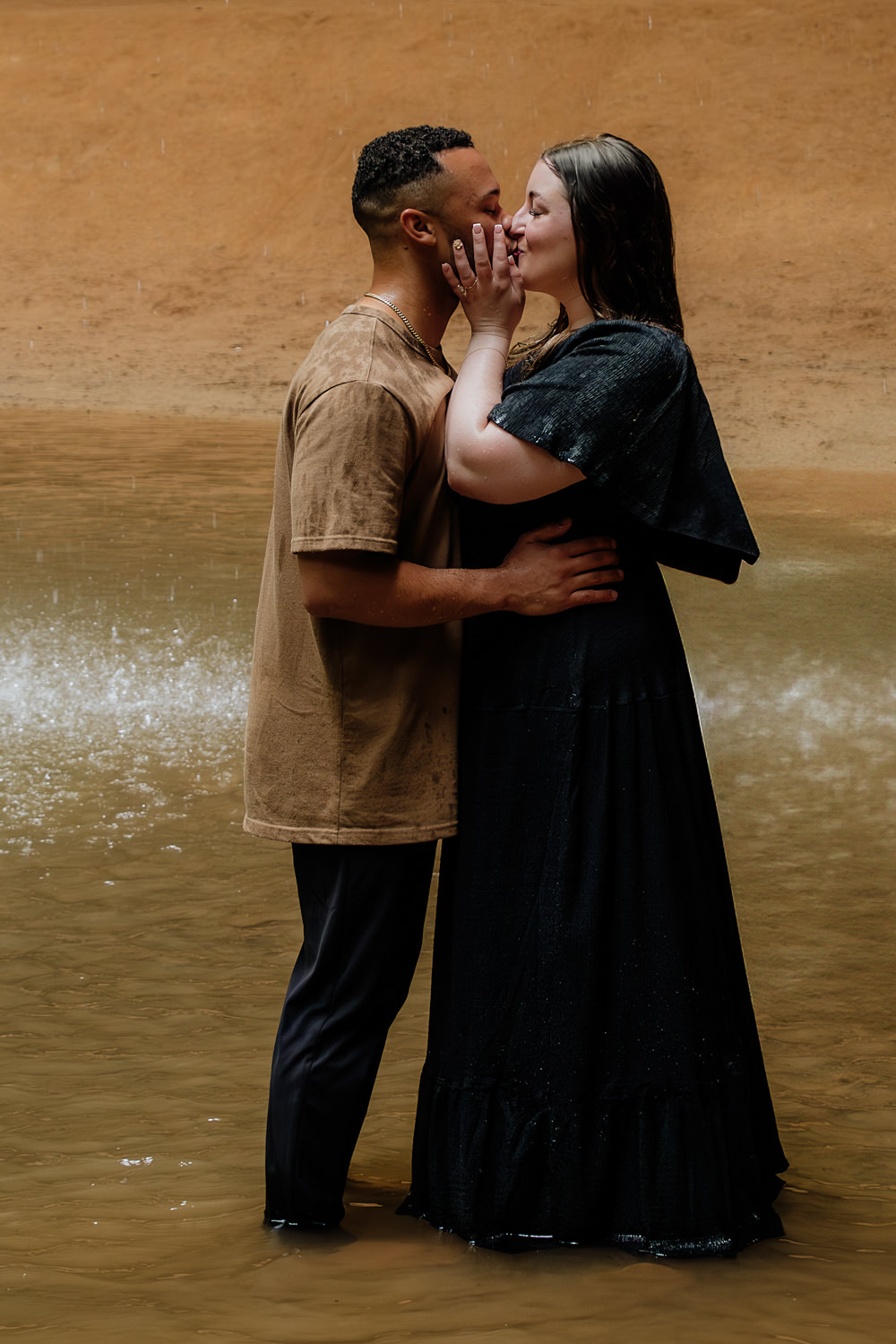A man and woman kiss underneath a waterfall in the Hocking Hills during an engagement session.
