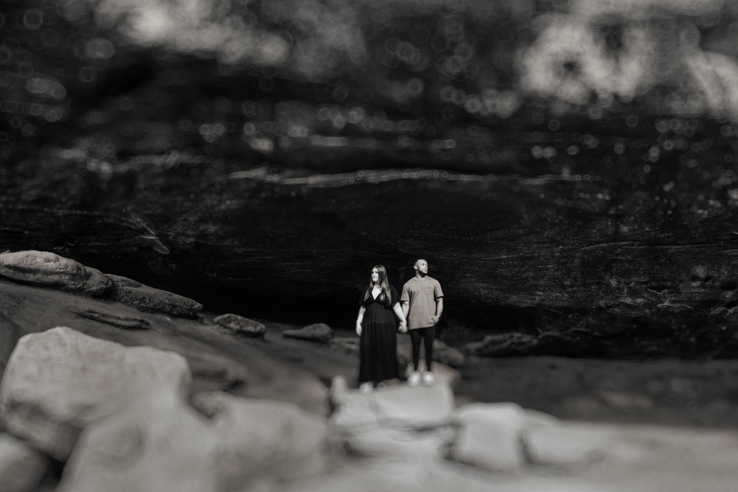 A wide angle black and white photo of a couple in Ash Cave with tilt shift vintage blur.