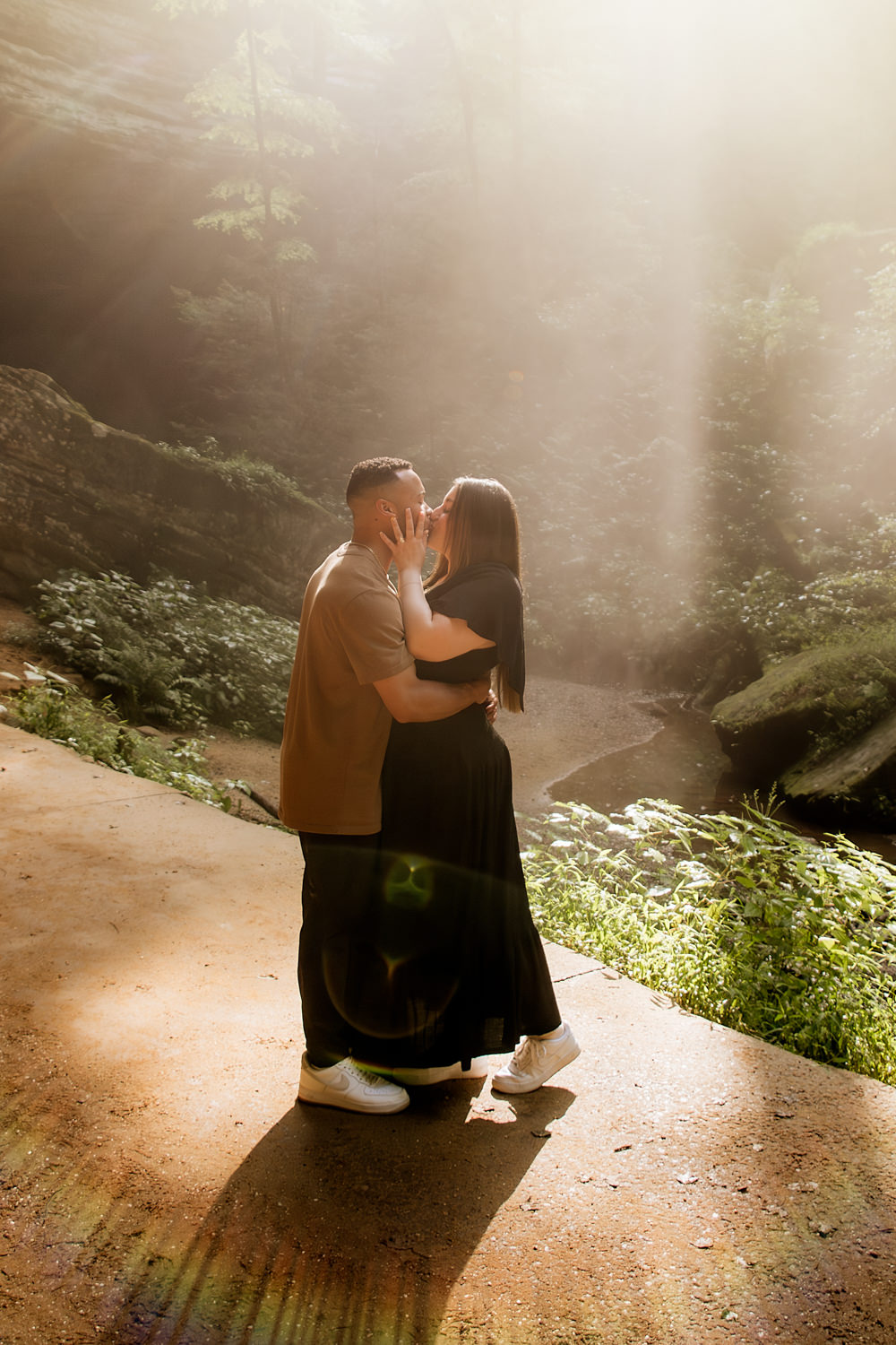 A couple leans in for a kiss as sun rays engulf them and a rainbow ray forms at their feet.
