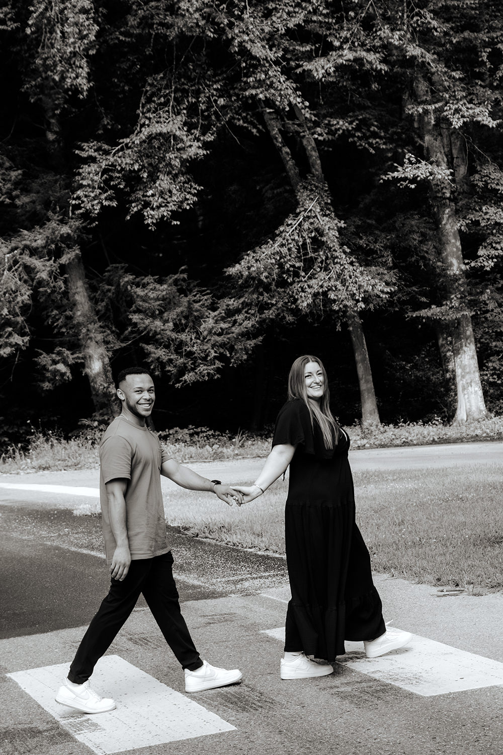 Black and white photo of a couple holding hands and crossing a crosswalk at Ash Cave in Hocking Hills, Ohio for their engagement session.