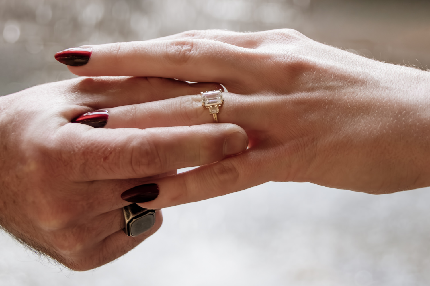 A man places an engagement ring on a woman's finger. In the background, the light catches droplets of water from a waterfall.