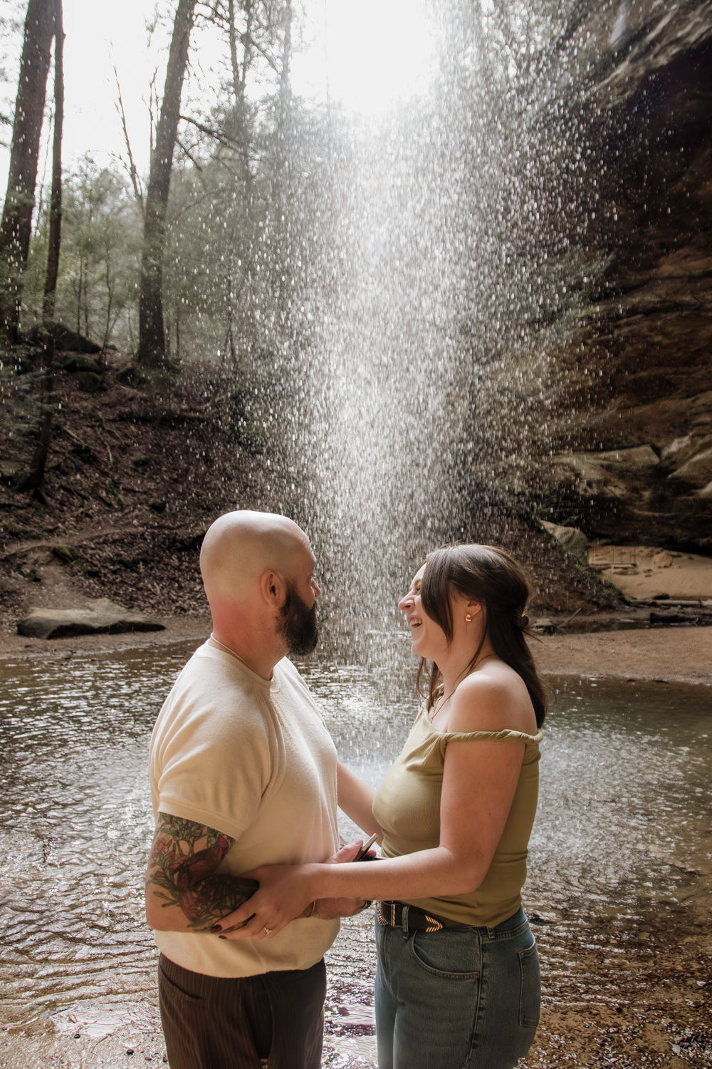 A woman and man embrace behind a waterfall in the Hocking Hills.
