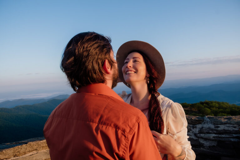 Full-length portrait of a wedding couple embracing on a rocky summit with layers of blue ridges waking up behind them.