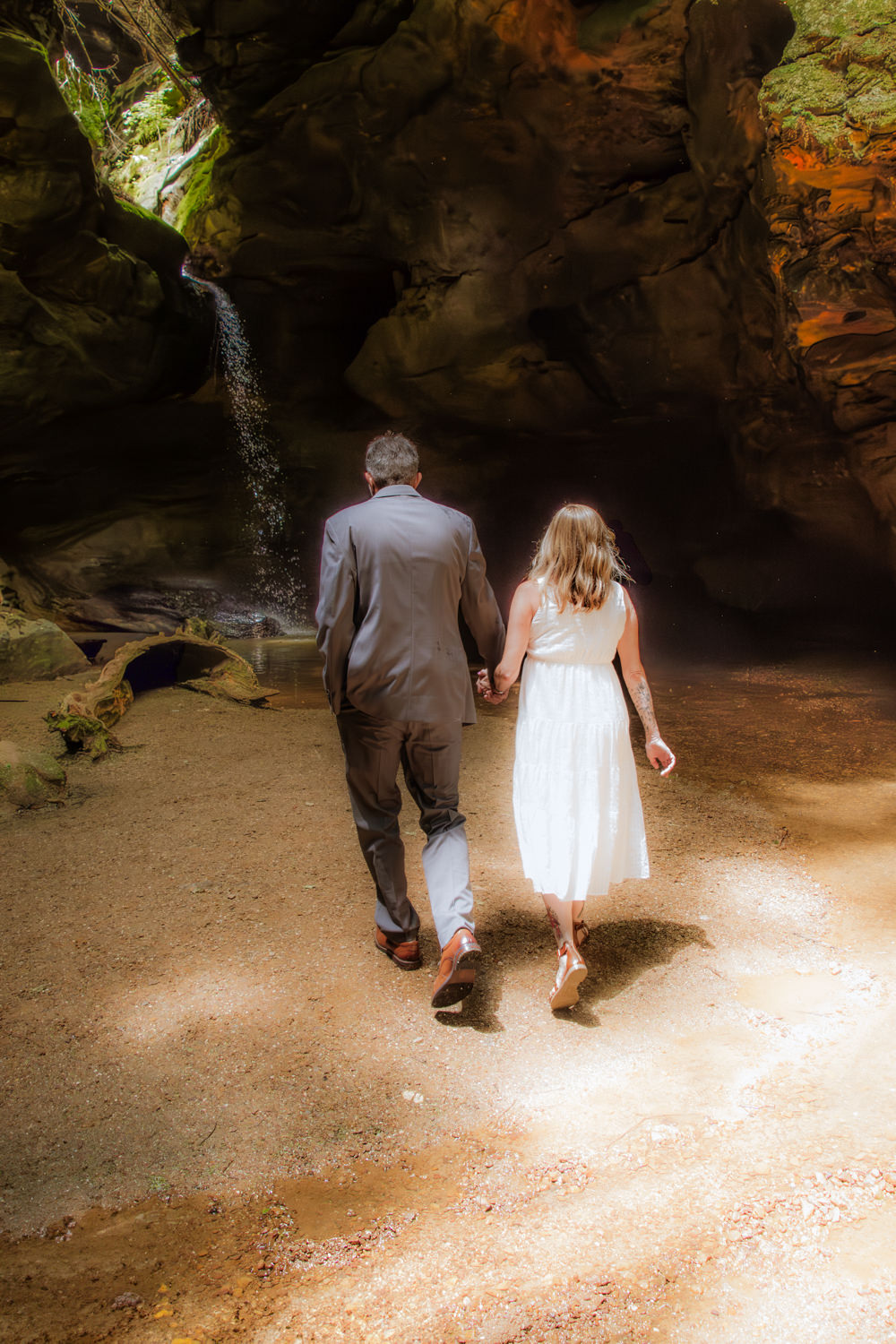 A couples walks away from the camera and towards Conkles hollow gorge waterfall.  The light is hazy and dreamy.