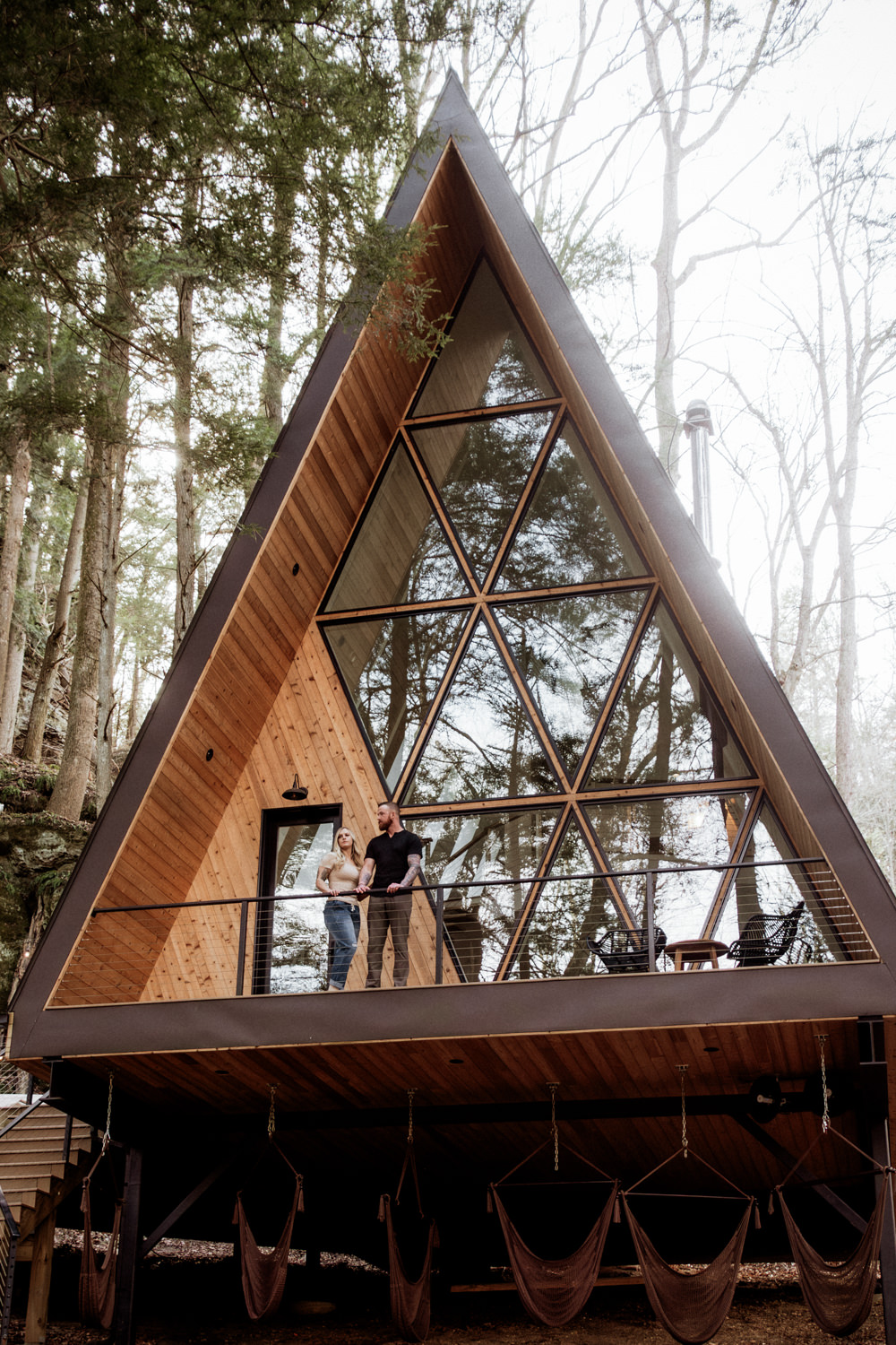 A woman and man pose on the balcony of an A-frame cabin in Ohio for their anniversary portraits. They traveled from North Dakota for their photo session.