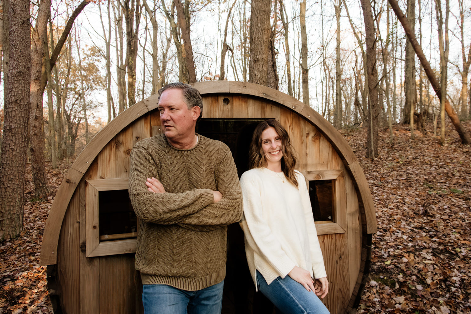 Full-length portrait of Taylor and Jeff dressed in cozy autumn sweaters, leaning against the sauna pod of The Pine at Dunlap Ridge.
