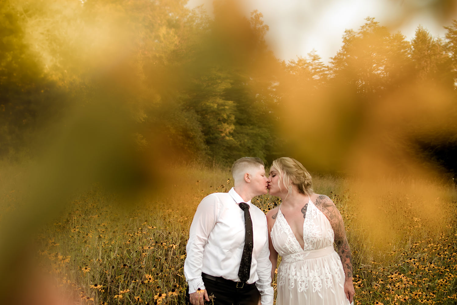 A queer couple stands in a vibrant yellow wildflower field in the Hocking Hills.