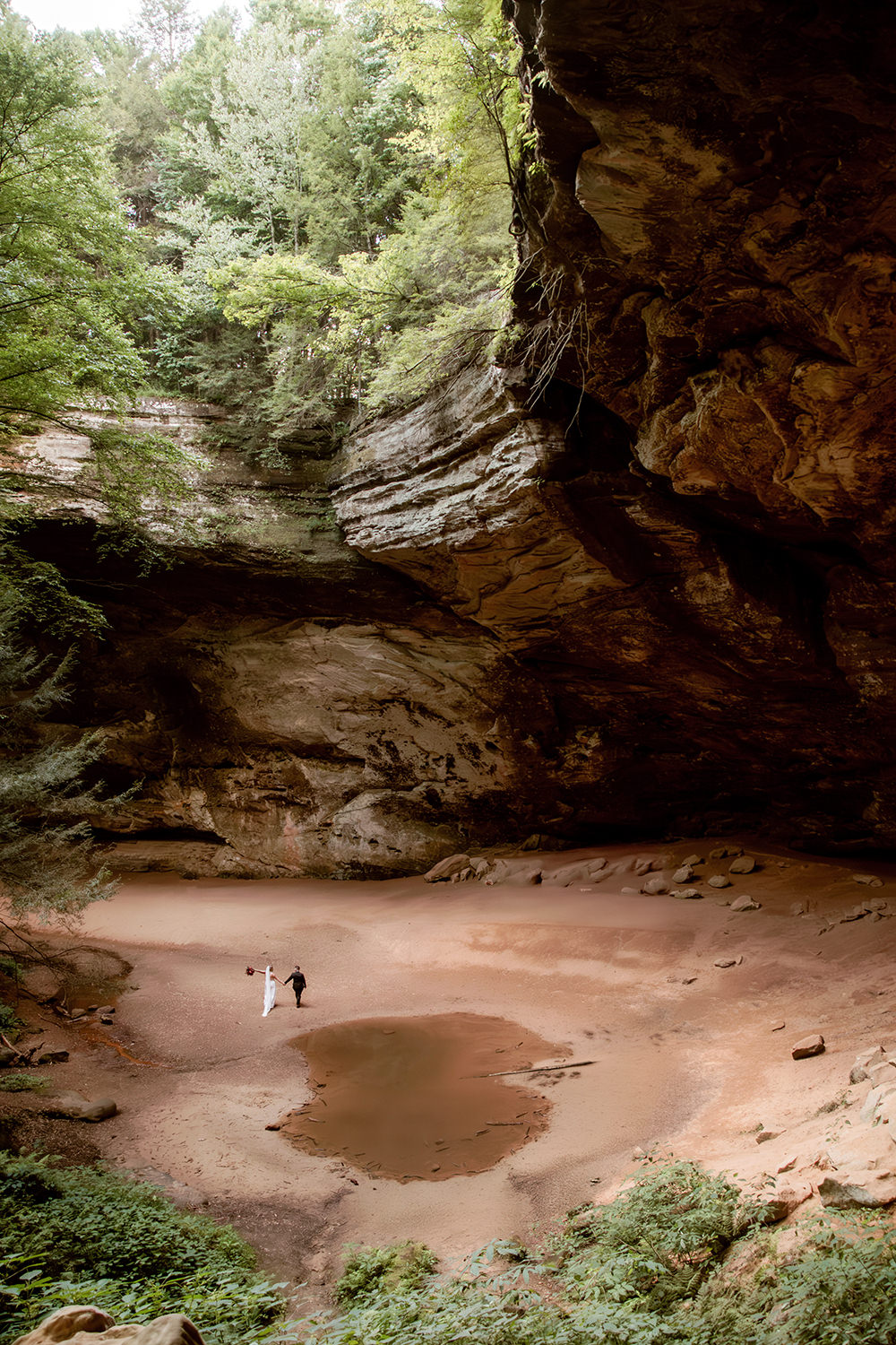 Epic wide shot of Ash Cave with a tiny couple by the water pool.