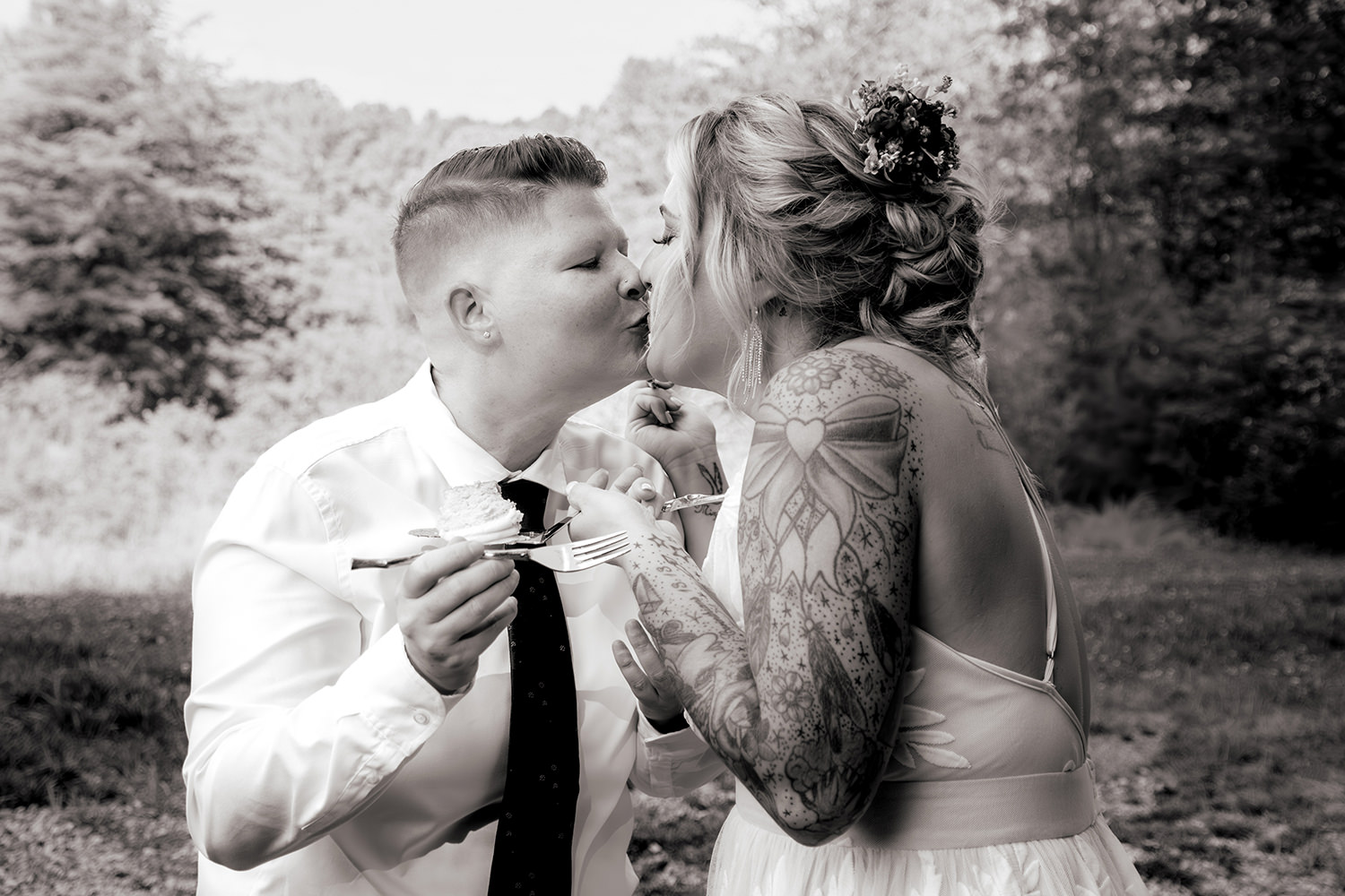 Black and white photo of two brides kissing after cutting their cake.