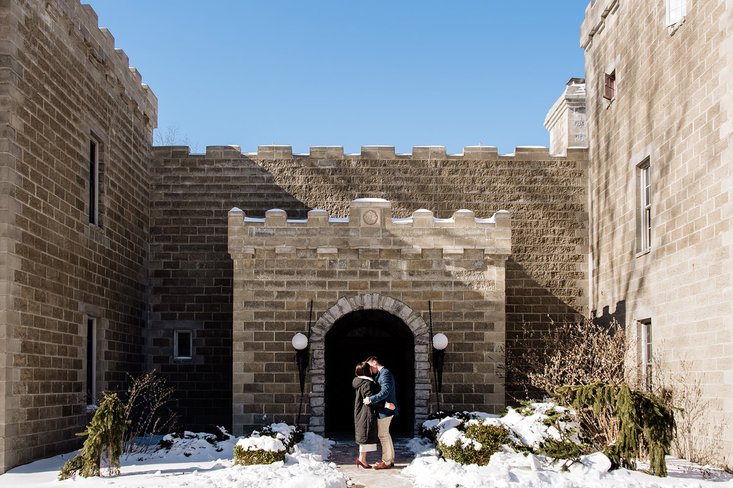 A couple embraces on the drawbridge at Ravenwood Castle in winter following a magical surprise proposal.