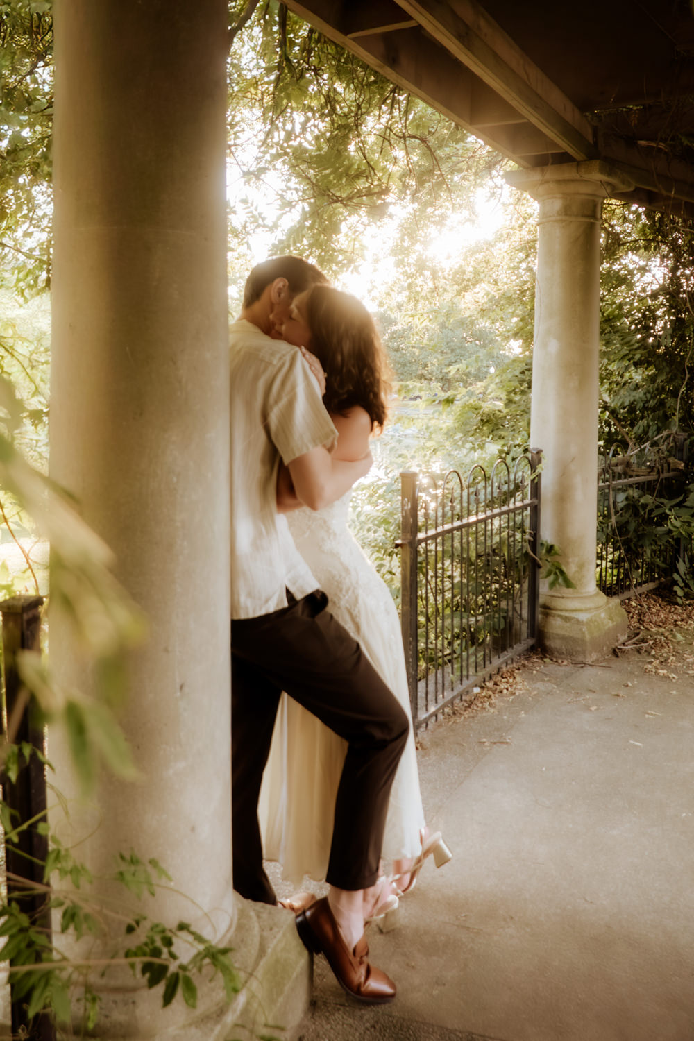 A man and woman have a sweet and romantic moment as they cuddle under an arbor in Schiller Park Columbus. The light is ethereal and artistically captured.