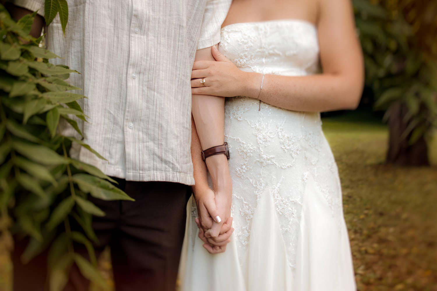 Closeup of a man and woman holding hands. The woman's other hand stretches across the man's arm and reveals an engagement ring.