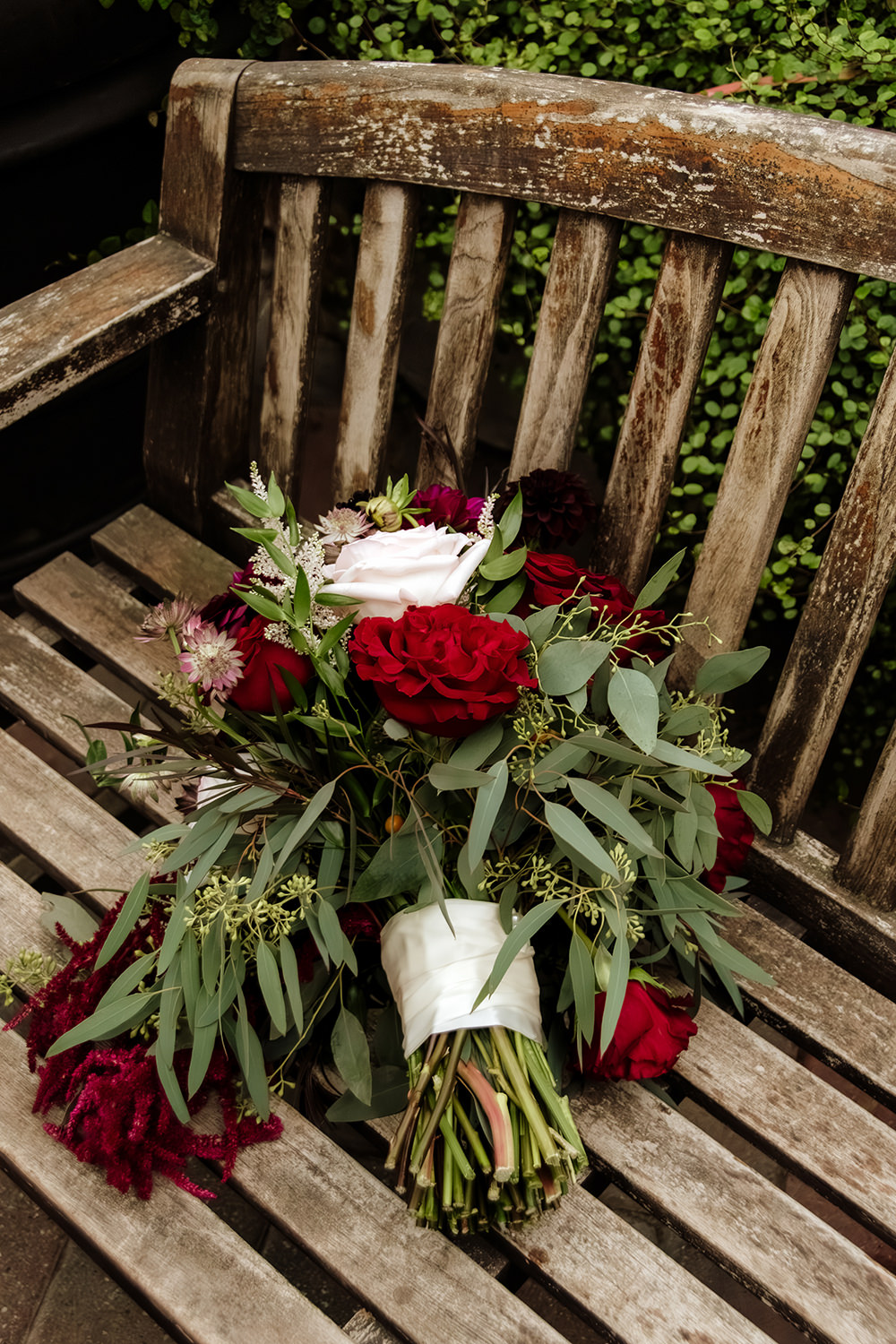 A bouquet of red and white roses sits on a conservatory park bench slick with rain.