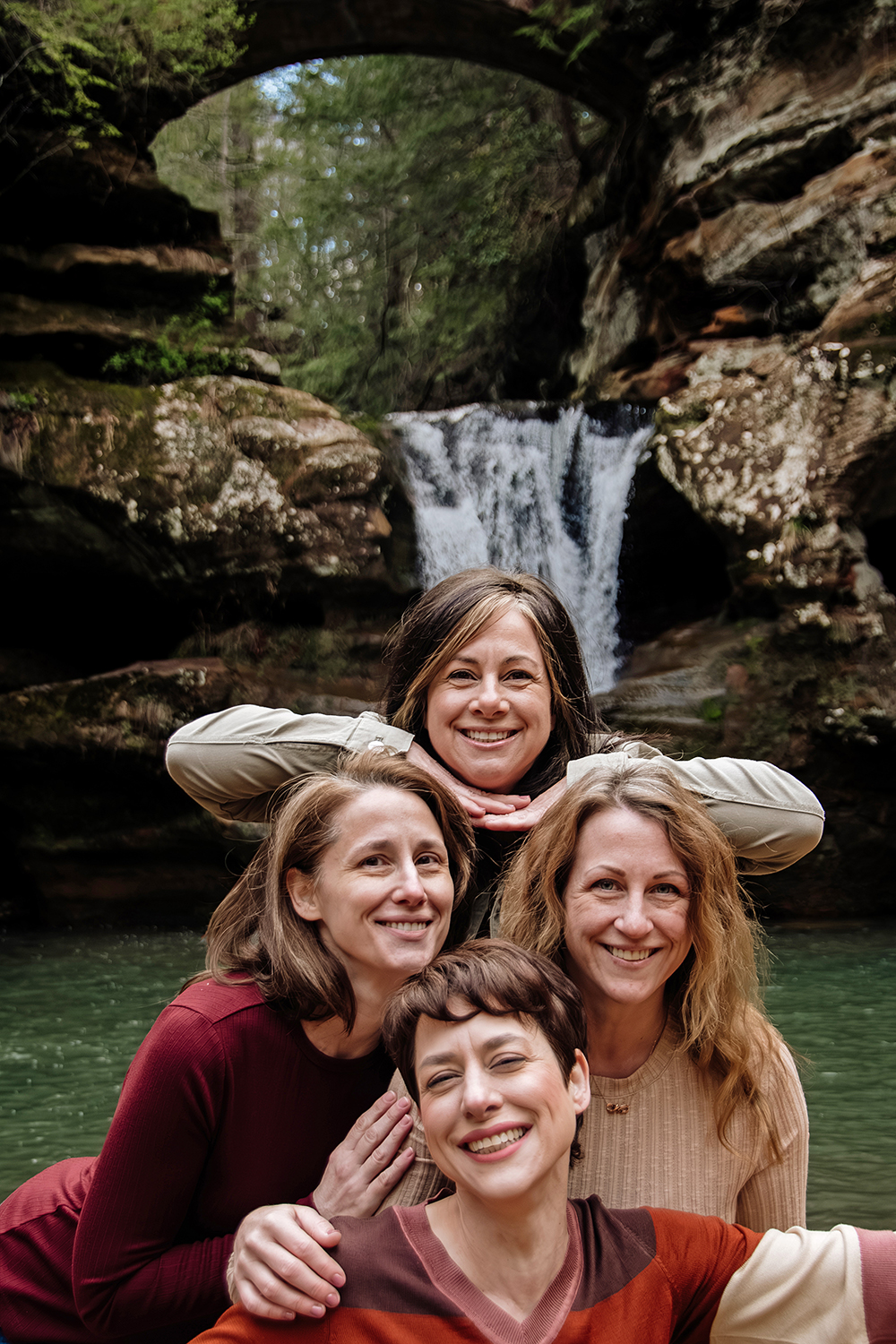 Four middle aged sisters link arms and skip towards the camera during an extended family session at Upper Falls.