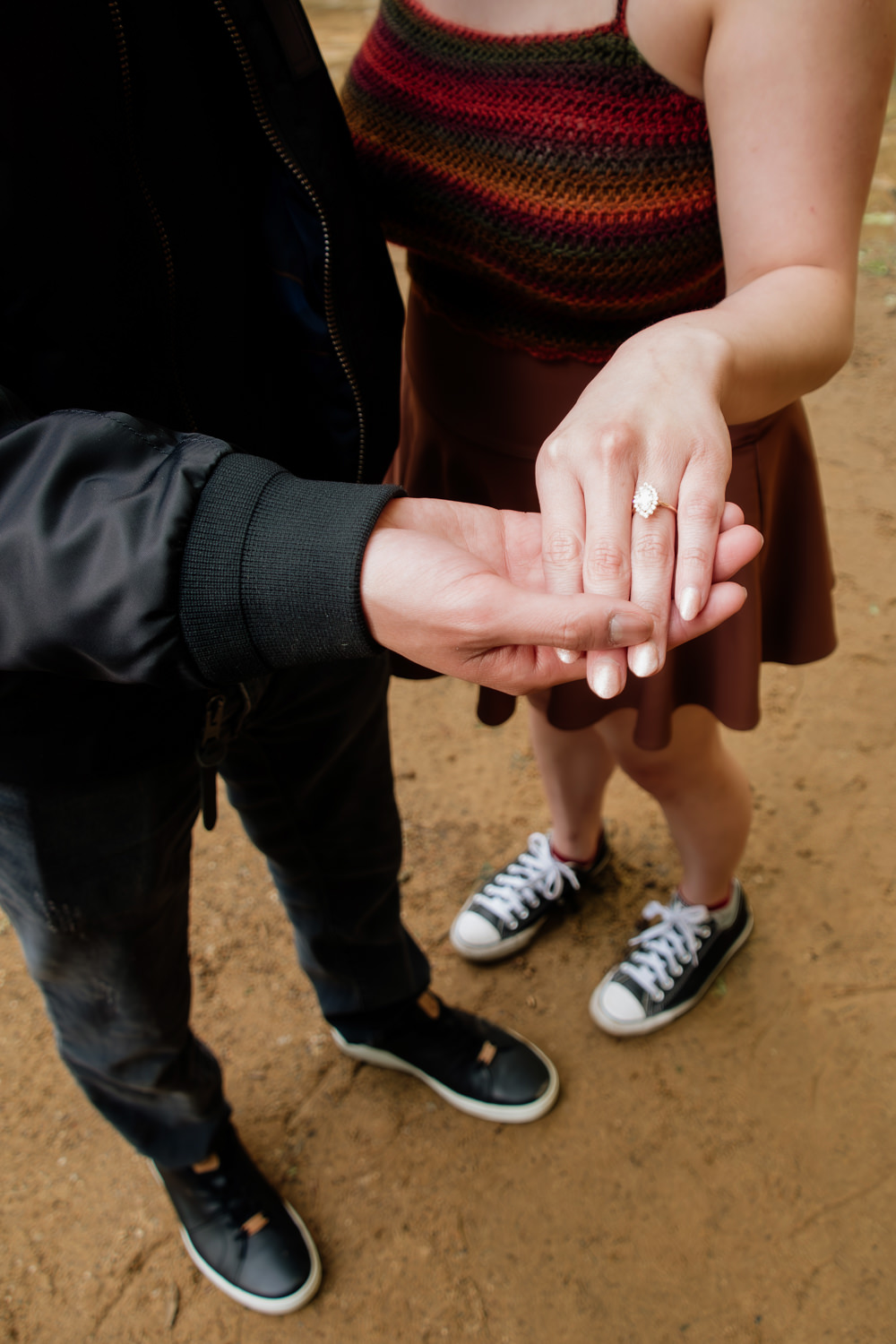 A man holds a woman's hand and shows off her new engagement ring.