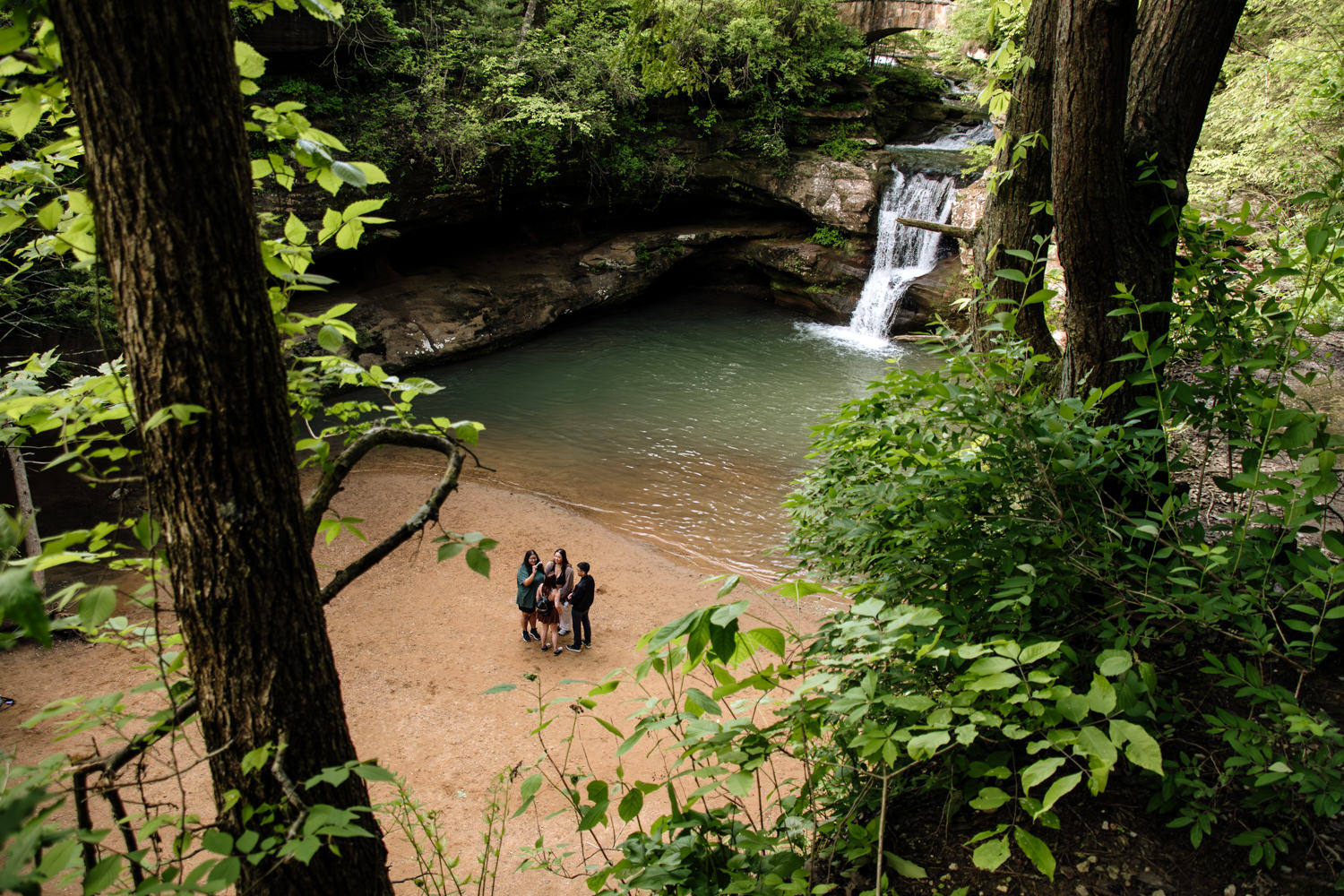 A wide overhead photo of a group of people standing in front of Upper Falls in the Hocking Hills. 