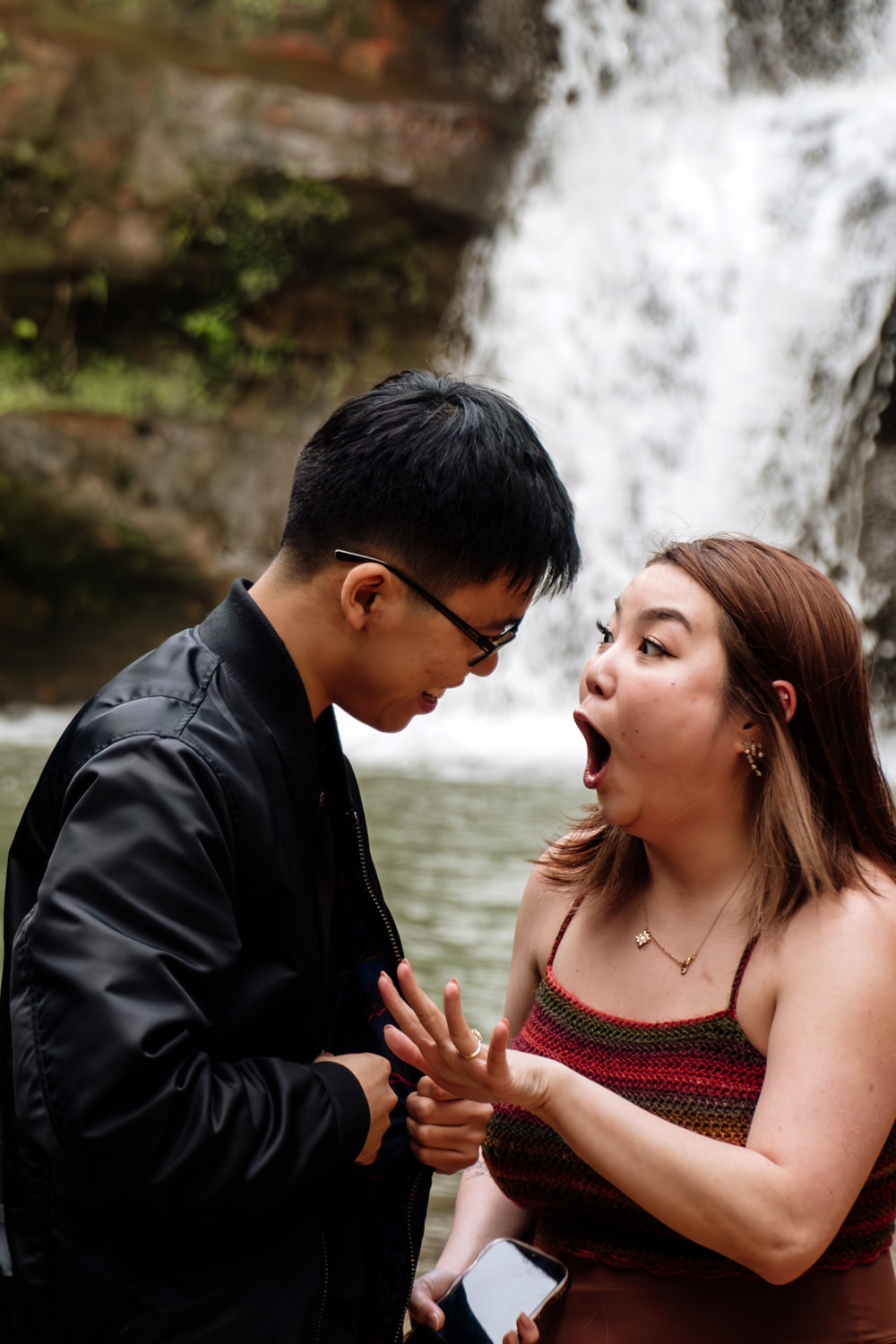 A woman holds up her hand and reacts after her boyfriend proposes.