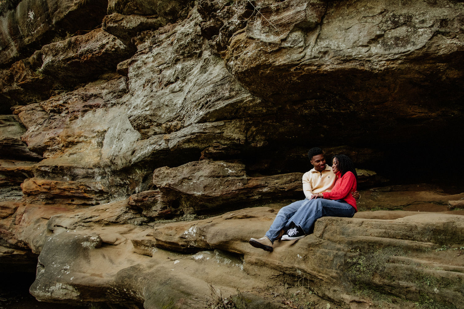 A black couple sits on a sandstone cliff after their proposal at Upper Falls in the Hocking Hills.