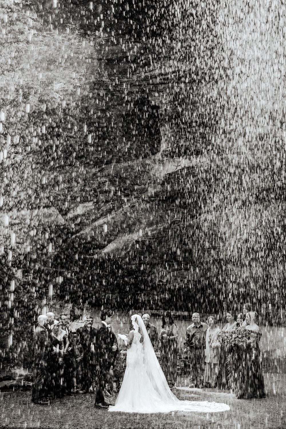 A unique perspective photo of a wedding ceremony at Ash Cave.  The ceremony is photographed through the waterfall and droplets are frozen in the frame.
