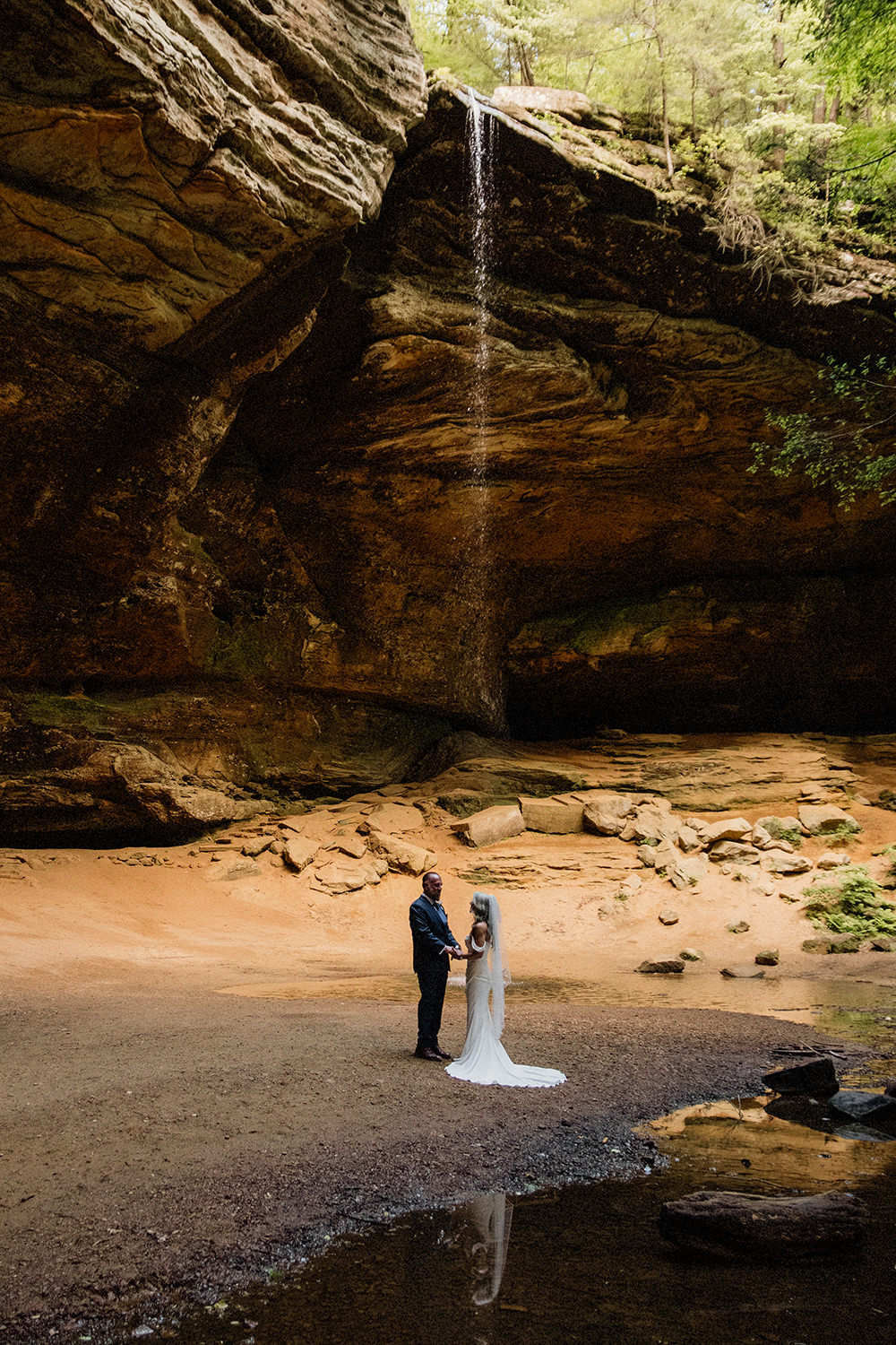 An elopement couple stands under the waning light at Ash Cave next to the waterfall.