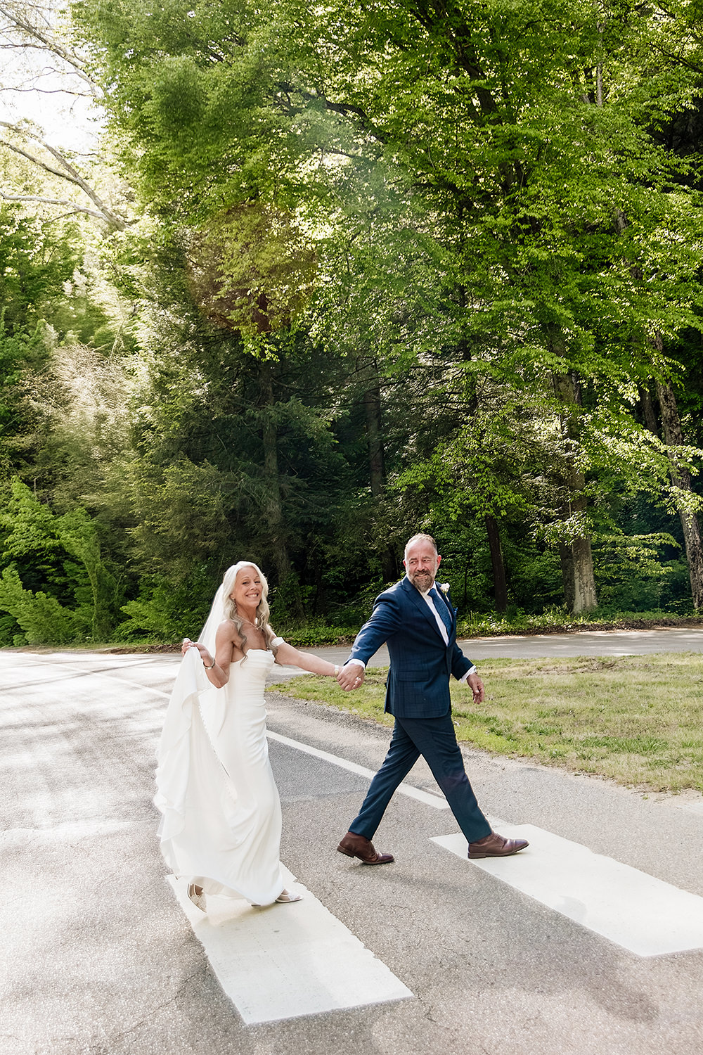A mature elopement couple holds hands and crosses the crosswalk at the Ash Cave trail in Hocking Hills on the way to their wedding vows.