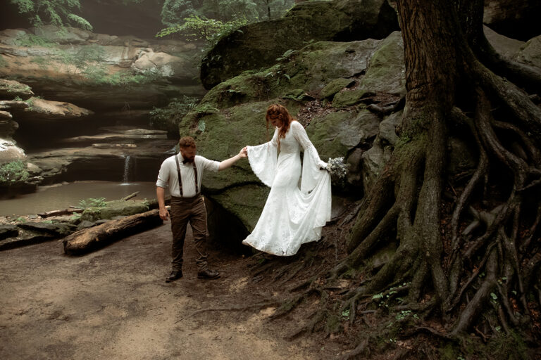Moody portrait of a couple walking in a deep green forest, their red hair and brown and cream attire perfectly complementing the natural landscape.