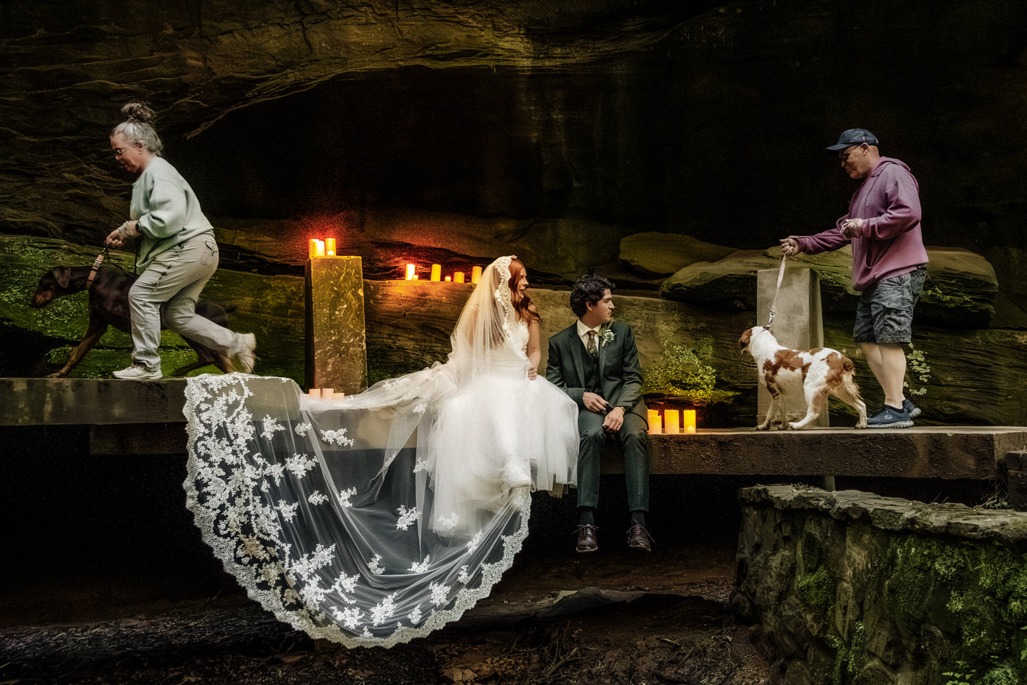 An elopement couple sits on a unique stone bridge at Old Man's Cave.  They are flanked in LED candles.  Vistors with dogs scoot by on the bridge.