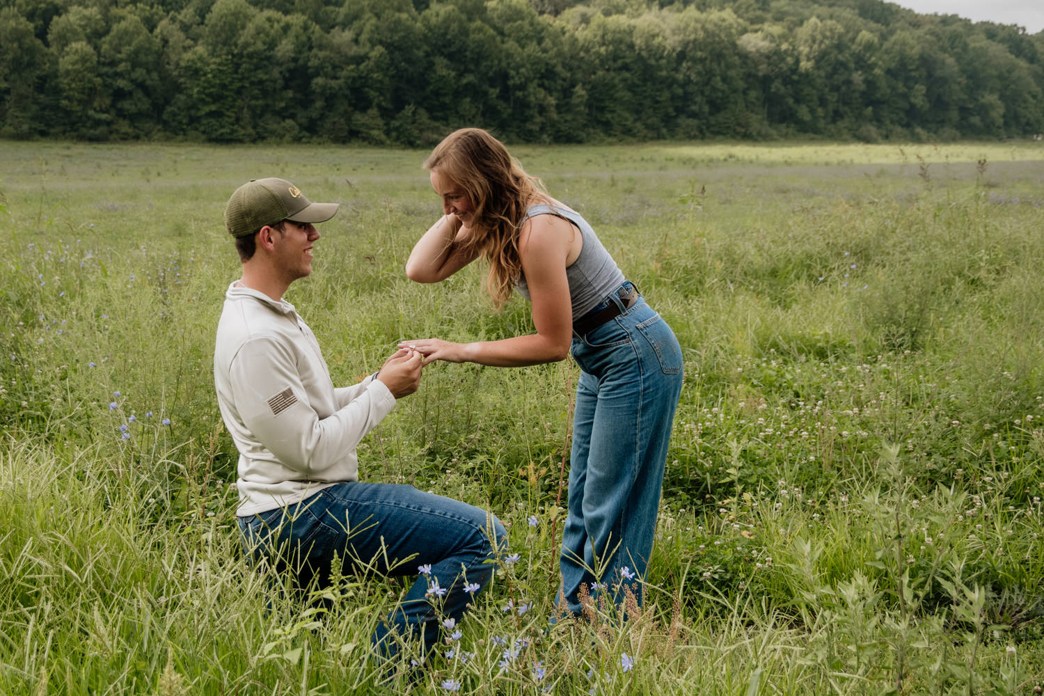 Man kneeling in a field of wildflowers to recreate his wedding proposal.