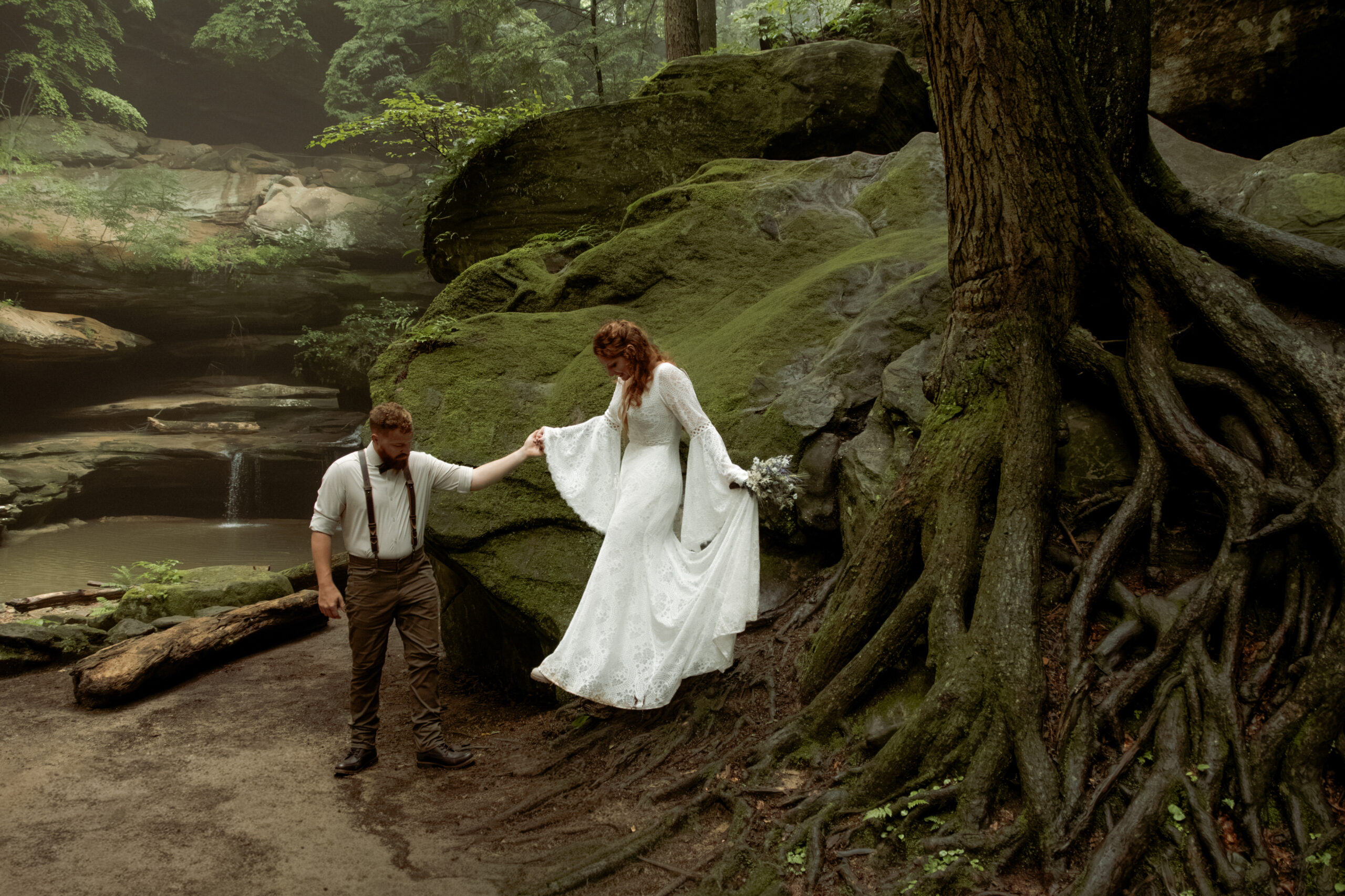 Beautiful foggy elopement next to tree roots, mossy rocks, and a waterfall in Old Man's Cave gorge in the Hocking Hills, Ohio.