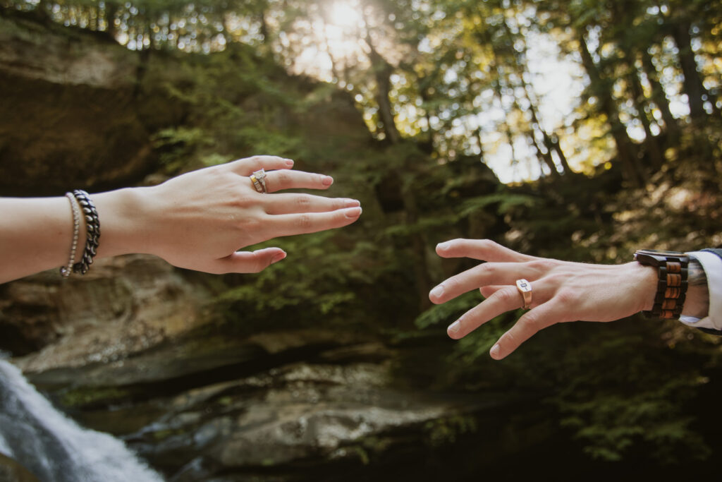 Hands reaching across a waterfall as light falls through the trees.