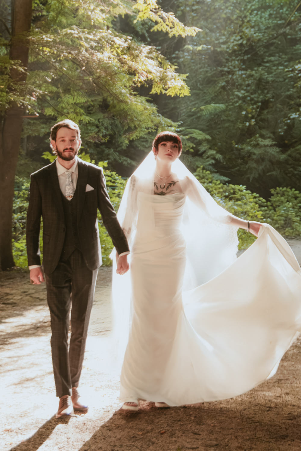 Bride and groom holding hands in front of a full-flowing waterfall in August.
