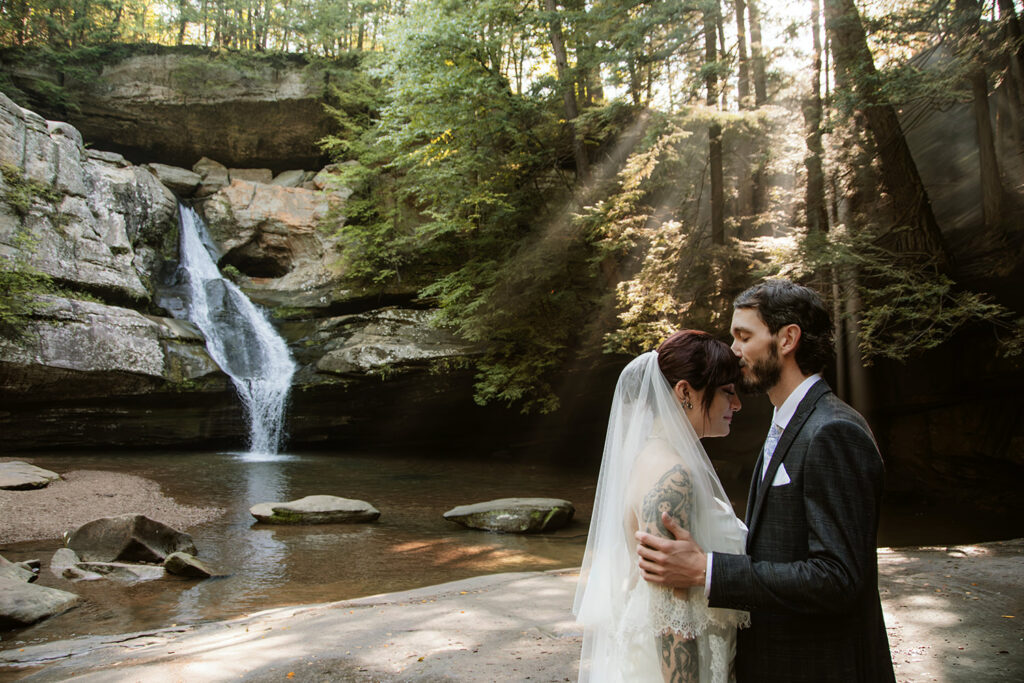Couple sharing their first kiss as husband and wife with Cedar Falls in the background.