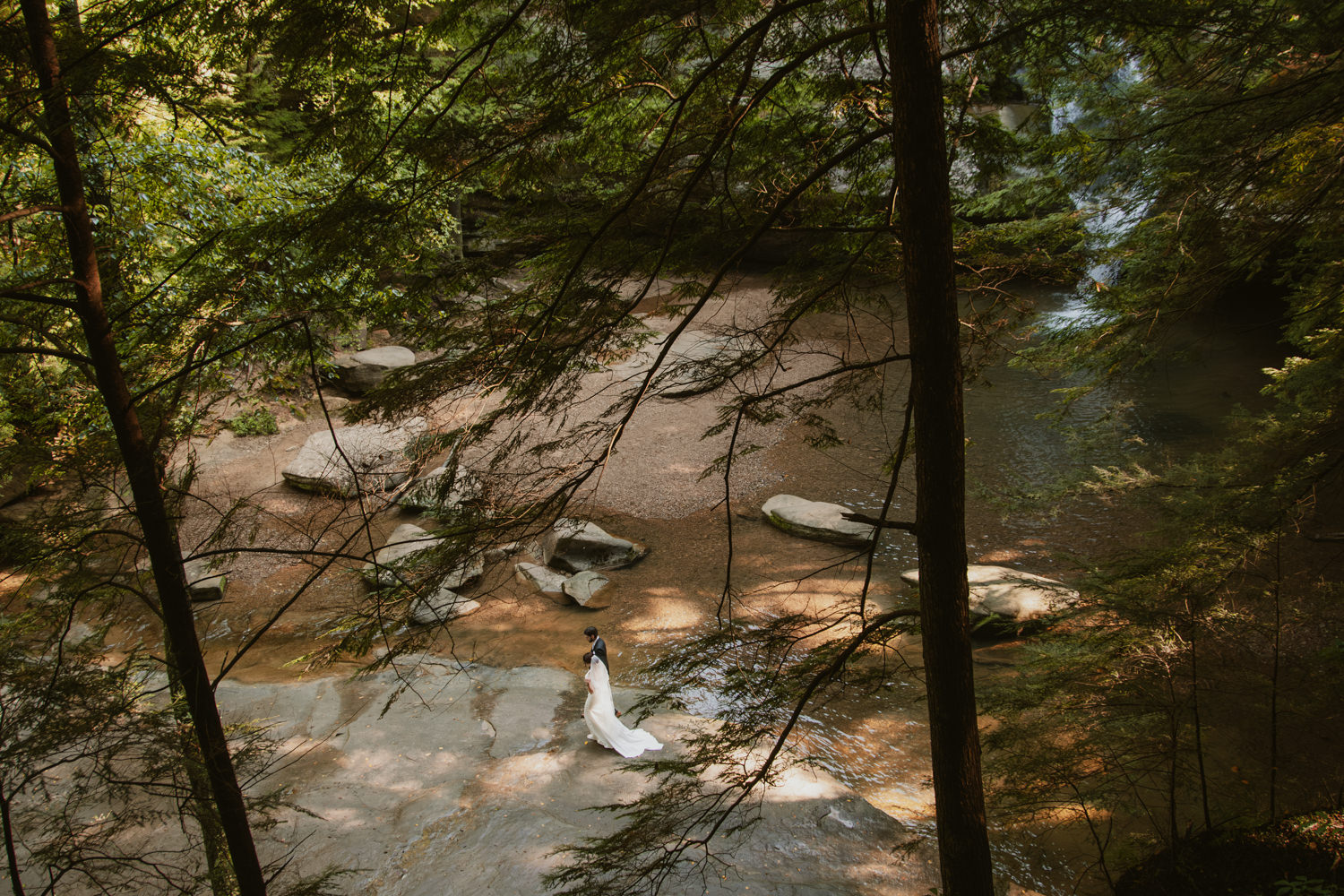 Wide portrait of couple standing on giant rock formations in a dramatic forest canyon.