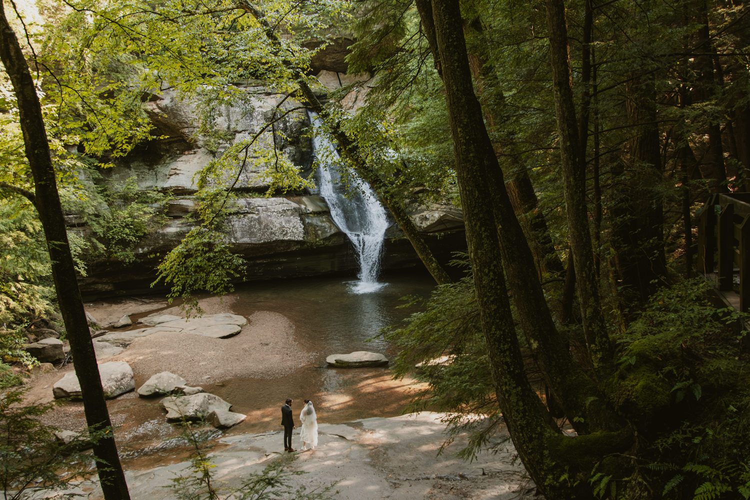 Bride and groom walking hand-in-hand along the wet stone trail following their ceremony.