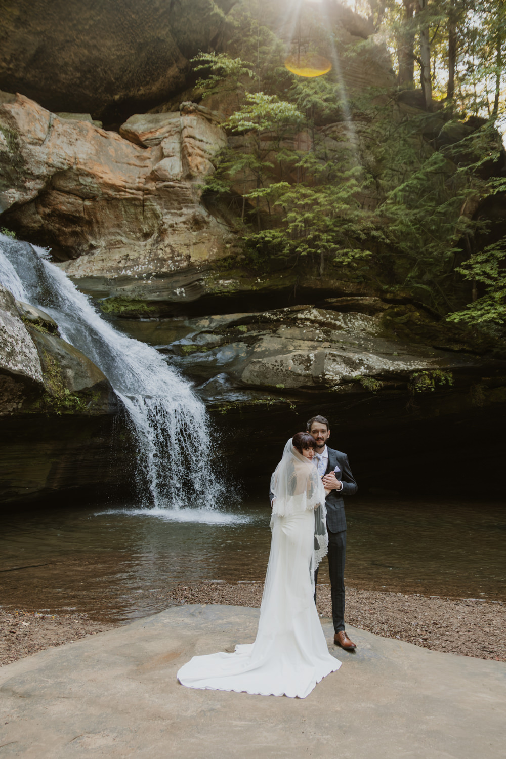 An elopement couple poses in front of a flowing waterfall in Hocking Hills.