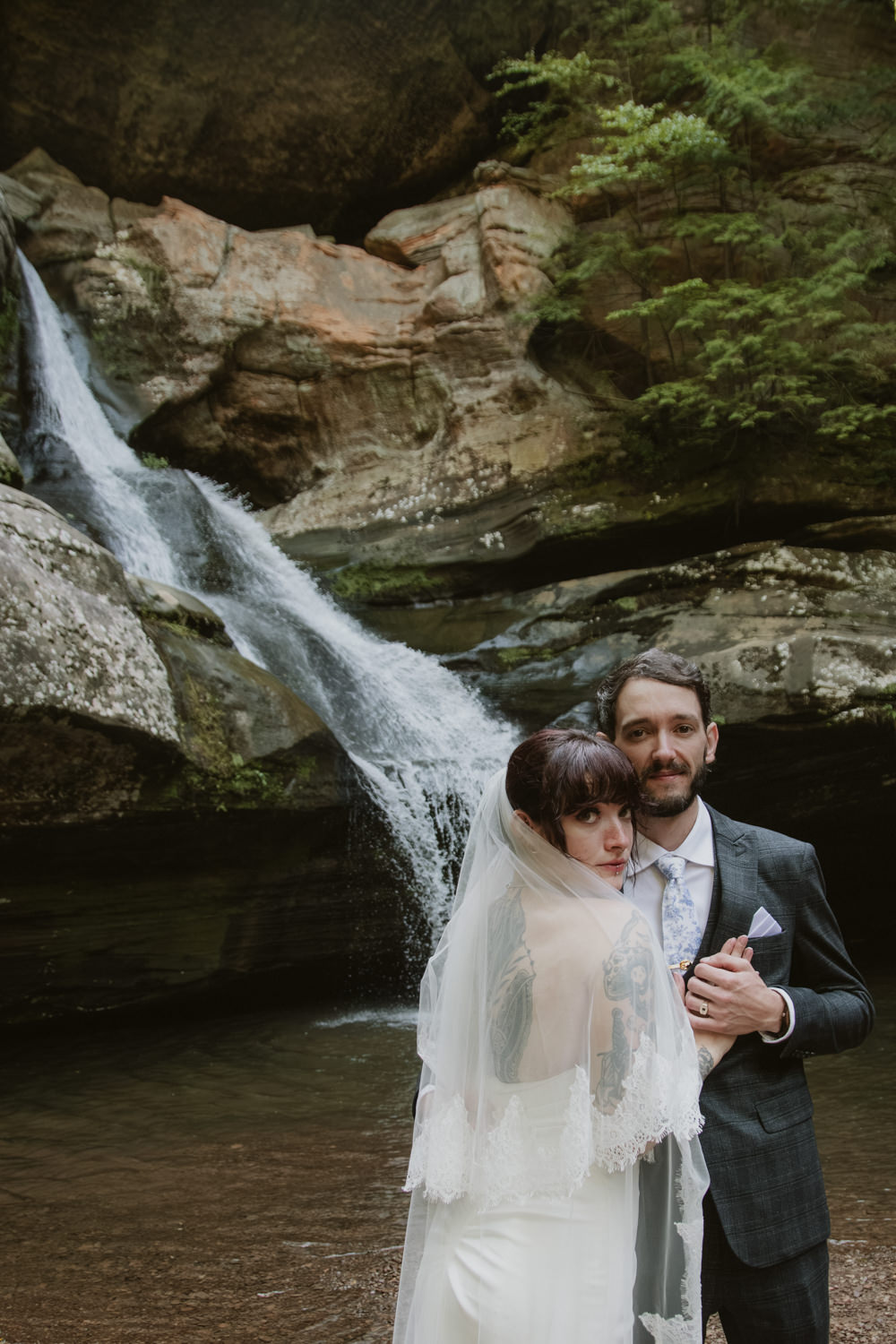 An elopement couple poses in front of a flowing waterfall in Hocking Hills.