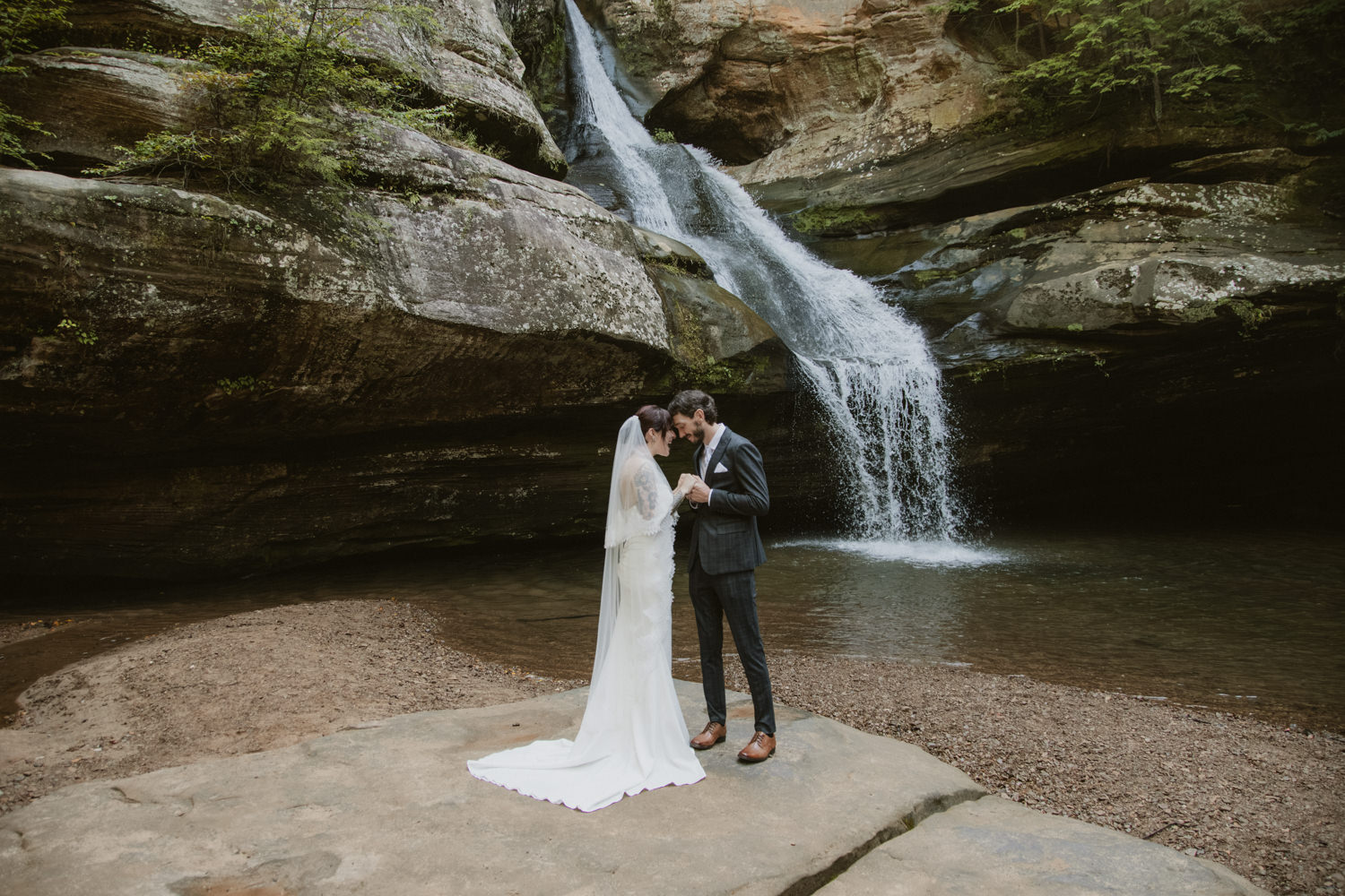 An elopement couple poses in front of a flowing waterfall in Hocking Hills.