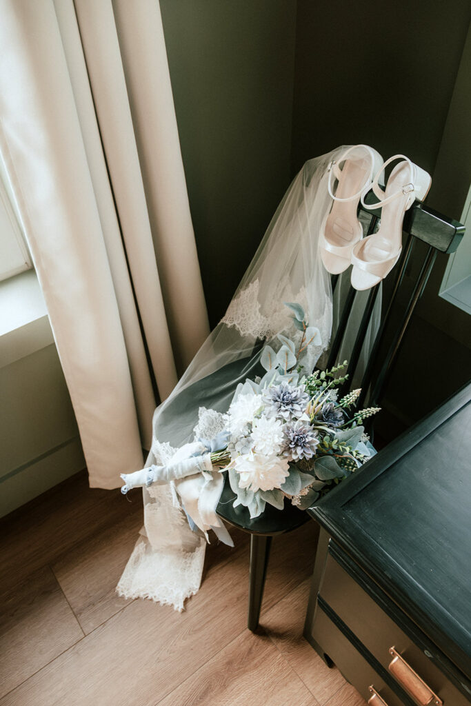Romantic detail photo of veil, bouquet, and shoes next to ethereal window light.