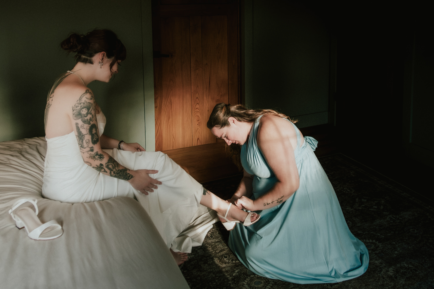 Maid of honor helping bride put on her shoes.