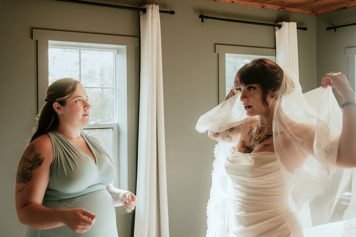 A bride puts on her veil with the help of her pregnant best friend maid of honor.