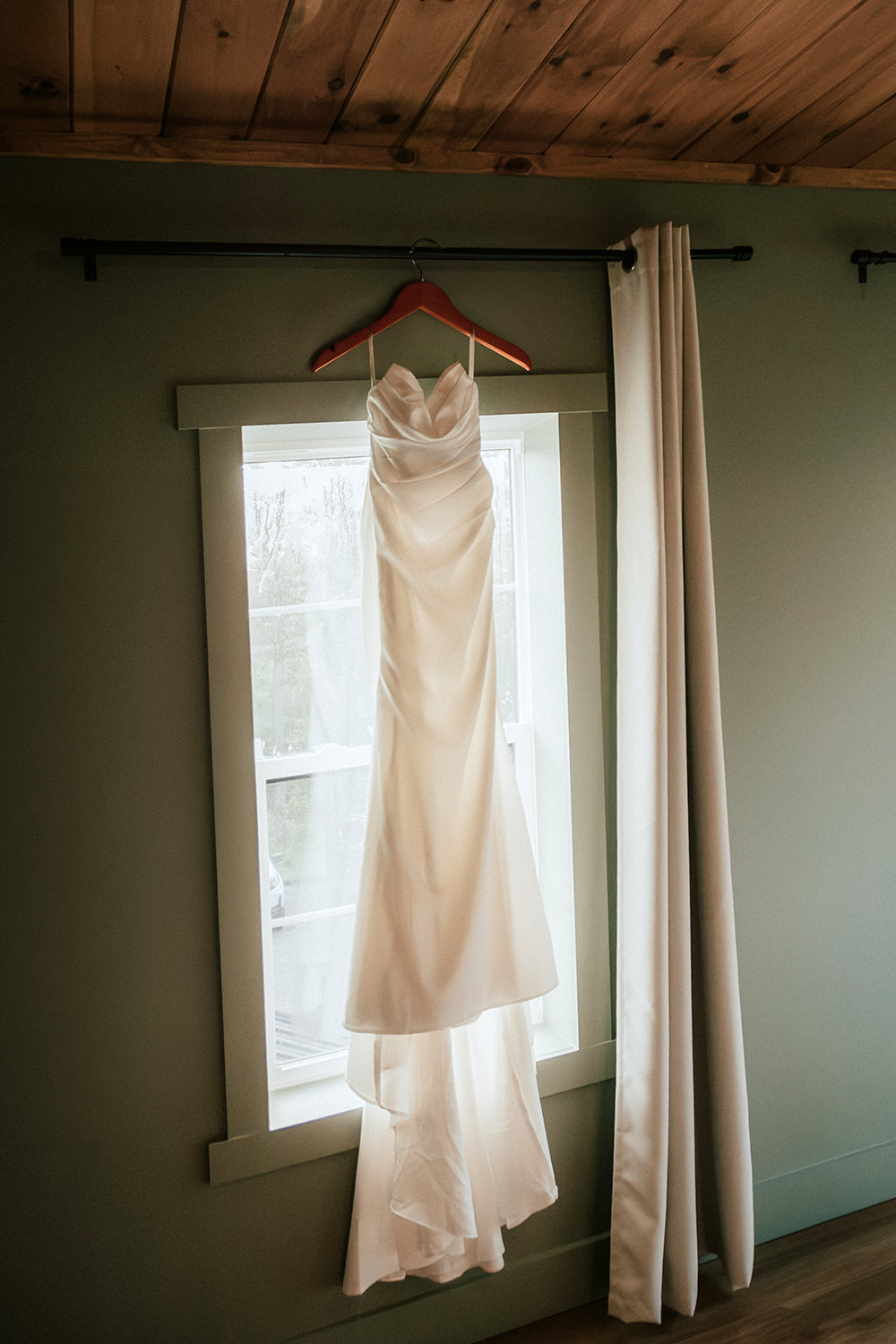 Bride's wedding dress hanging against a rustic wooden log cabin wall.