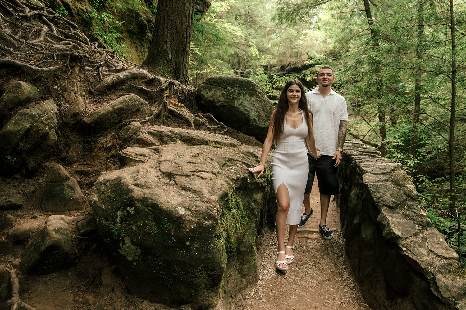 Anthony holding Alethia’s hands as they look at each other surrounded by tall hemlock trees in Logan, Ohio.