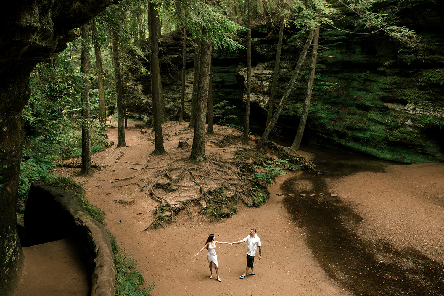Alethia and Anthony embrace in front of the sweeping sandstone cliffs and green foliage at Old Man’s Cave.